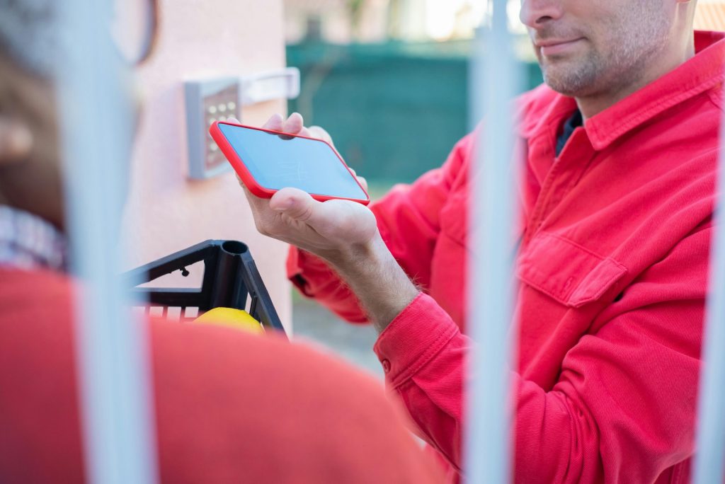 Un livreur en veste rouge utilise un smartphone pour confirmer la livraison d'un colis.