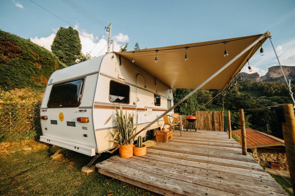 Camping confortable en caravane avec terrasse en bois et plantes en pot donnant sur un paysage pittoresque.